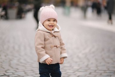 Şehrin ortasında kahverengi kot pantolon ve pembe şapka giyerek gülümseyen küçük bir kız çocuğu. Sevimli küçük kız.