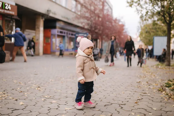 아름다운 갈색 코트를 입고 도시를 걷고 있는 사랑 스러운 작은 소녀. 귀엽고 11 개월된 아기가 웃고 뛰어요 — 스톡 사진