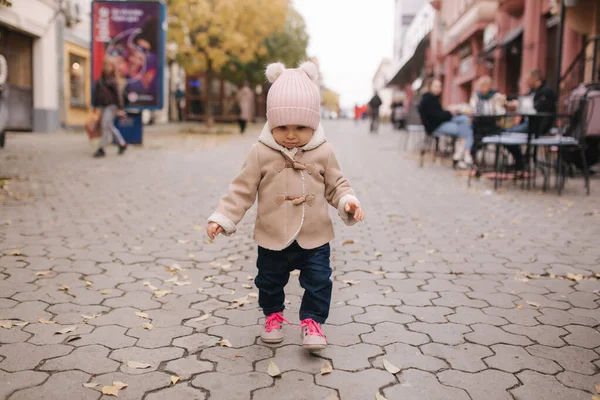 Imádnivaló kislány, gyönyörű barna kabátban sétál a városban. Aranyos tizenegy hónapos baba mosoly és fuss — Stock Fotó