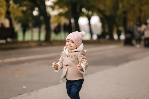 Pequeno bebê onze meses andando no parque. Bebê feliz em casaco marrom bonito, chapéu rosa e jeans jeans jeans — Fotografia de Stock