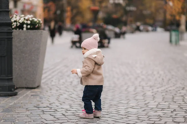 Gelukkige baby meisje wandelen in de stad in de herfst tijd. Leuke baby in bruine jas en jeans — Stockfoto