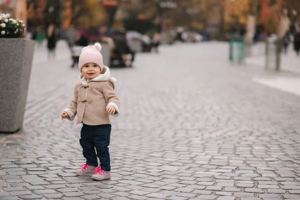 Boldog kislány sétál a városban ősszel. Aranyos baba barna kabátban és farmerban. — Stock Fotó