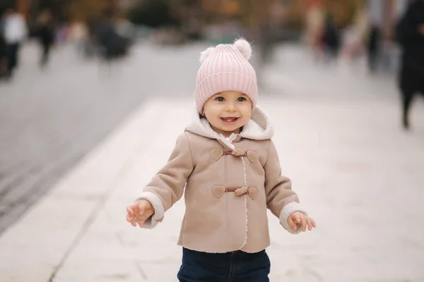 갈색 코트 데님 예지앤 핑크 모자를 쓴 작은 소녀가 웃으며 도시 중심에 서 있었다. 귀여운 귀염둥이 — 스톡 사진
