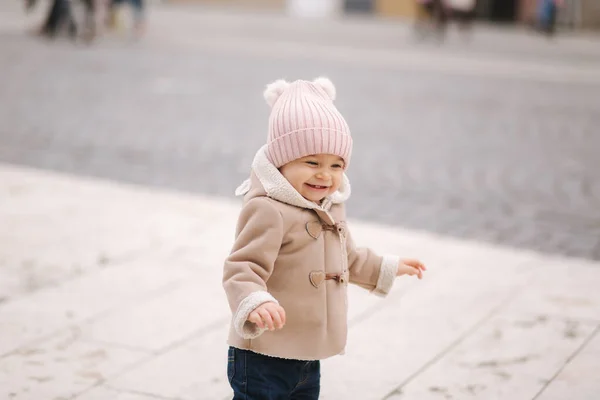 Happy baby girl walking in the city in autumn time. Cute baby in brown coat and jeans — Stock Photo, Image