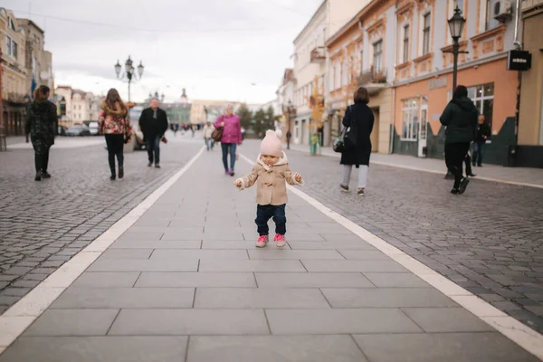 Happy baby girl walking in the city in autumn time. Cute baby in brown coat and jeans — Stock Photo, Image