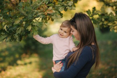 Parktaki güzel ailenin portresi. Anne ve kızı sonbaharda bir araya gelirler. Güzel on aylık bebek annesinin ellerinde.