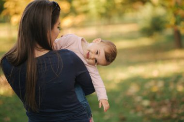 Parktaki güzel ailenin portresi. Anne ve kızı sonbaharda bir araya gelirler. Güzel on aylık bebek annesinin ellerinde.