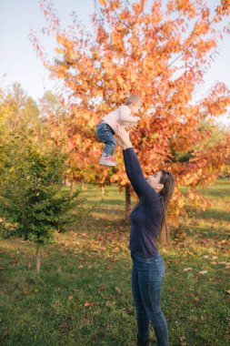 Mutlu, genç bir annenin bebeğini kucağına alıp ona sevgiyle bakışının yan görüntüsü. Sonbahar fotosistemi