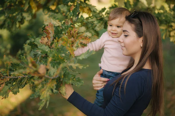 Ritratto di bella famiglia nel parco. Mamma e figlia insieme in autunno. Bellissimo bambino di dieci mesi sulle mani delle madri — Foto Stock