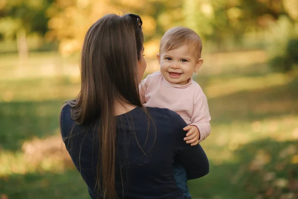 Portret pięknej rodziny w parku. Mama i córka spotykają się jesienią. Piękne 10-miesięczne dziecko na rękach matek — Zdjęcie stockowe