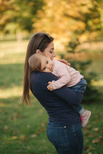 Portrait of beautiful family in the park. Mom and daughter togehter in autumn. Beautiful ten month baby on mothers hands