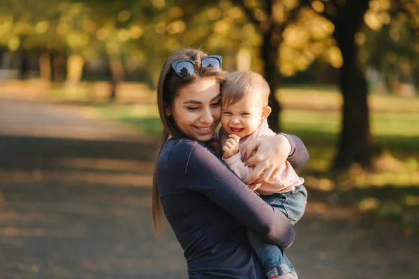 Очаровательная смеющаяся девочка на маминых руках в осеннем парке. Ближе к матери и дочери. Счастливая семья — стоковое фото