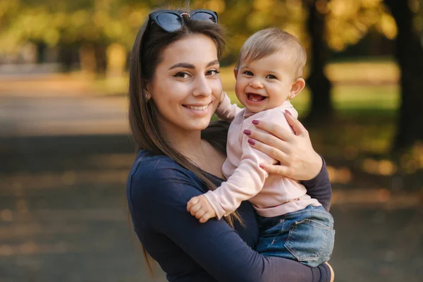 Adorable laughing baby girl on moms hands in autumn park. Close up on mother and daughter. Happy family — ストック写真