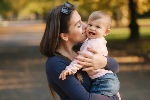 Adorable laughing baby girl on moms hands in autumn park. Close up on mother and daughter. Happy family — Stock Photo, Image