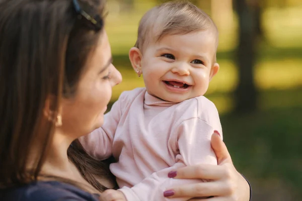 En söt skrattande liten flicka på mammas händer i höstparken. Närbild på mor och dotter. Lycklig familj — Stockfoto