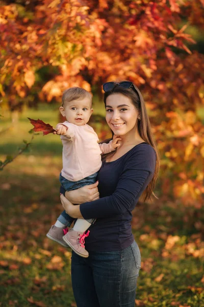Η μητέρα με το κοριτσάκι της στέκονται μπροστά στο κόκκινο δέντρο. Φθινοπωρινό πάρκο — Φωτογραφία Αρχείου