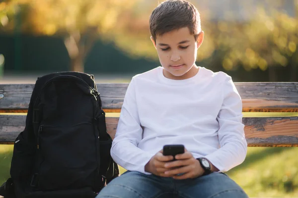 Adolescente menino jogar jogos online em seu smartphone no parque depois de aulas na escola — Fotografia de Stock