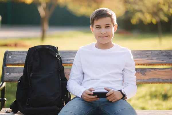 Adolescente menino jogar jogos online em seu smartphone no parque depois de aulas na escola — Fotografia de Stock