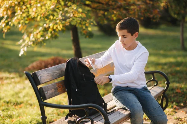 Przystojny nastolatek bierze z plecaka powerbark za ładowanie smartfona. Cute boy w parku w czasie jesieni — Zdjęcie stockowe