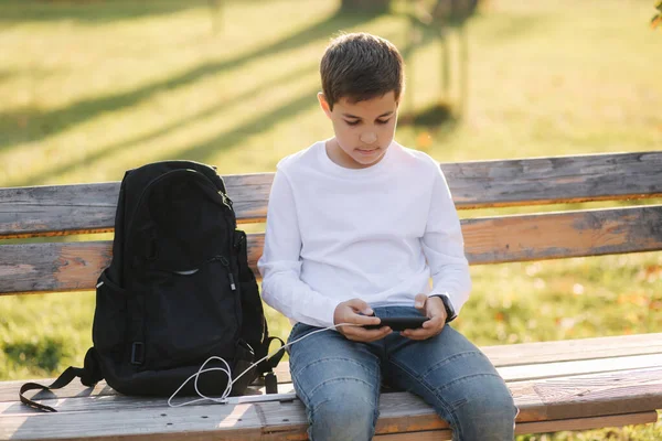 Ragazzo giocare giochi online su smartphone e utilizzando powerbank per la ricarica. Bello adolescente uso telefono otside — Foto Stock