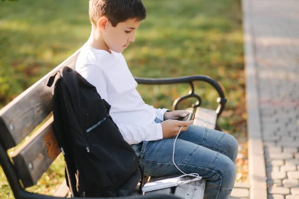 Ragazzo giocare giochi online su smartphone e utilizzando powerbank per la ricarica. Bello adolescente uso telefono otside — Foto Stock