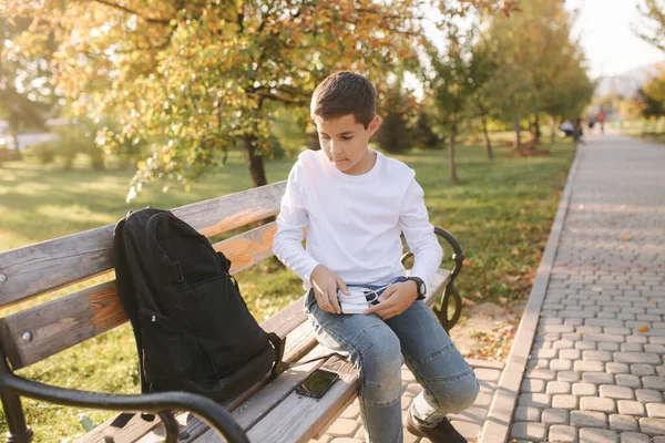 Guapo adolescente tomar de su mochila powerbark para cargar el teléfono inteligente. Lindo chico en el parque en otoño — Foto de Stock