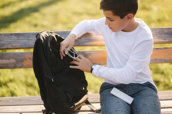 Pohledný teenager si vezme z batohu štěkot za nabíjení chytrého telefonu. Roztomilý chlapec v parku v podzimním čase — Stock fotografie