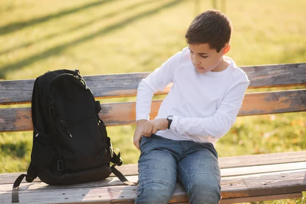 Jovem rapaz tirar do seu smartphone bolso. Adolescente sentado no banco no parque — Fotografia de Stock
