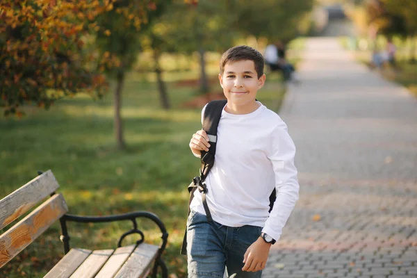 Školák chodí ráno do školy. Šťastný teenager v bílé košili s černým batohem jít studovat — Stock fotografie