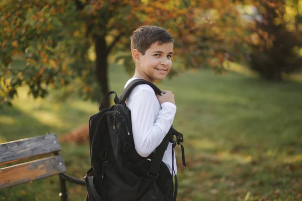 Aranyos tinédzser fiú hátizsákkal áll a parkban és várja a barátait. Arany ősz. Iskolásfiú — Stock Fotó