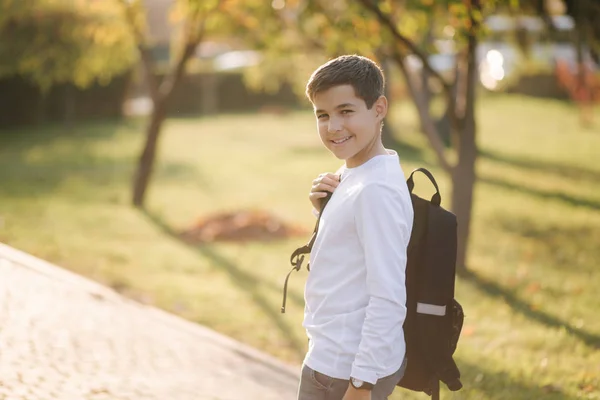 Widok nastoletniego chłopca idącego do szkoły. Młody mężczyzna w białej bluzie z plecakiem przejdź przez park — Zdjęcie stockowe