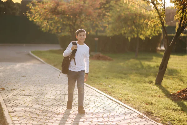 Happy schoolboy go back home after lessons. Teenager in white shirt denim jeans with backpack