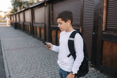 Genç çocuk kablosuz kulaklığı çıkarıp kulaklıklara takıyor. Sırt çantalı beyaz gömlekli genç bir çocuk. Çocuk müziği dinle.