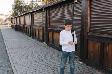 Genç çocuk kablosuz kulaklığı çıkarıp kulaklıklara takıyor. Sırt çantalı beyaz gömlekli genç bir çocuk. Çocuk müziği dinle.