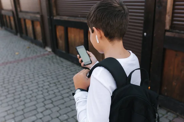 Makieta nastolatka ze słuchawkami bezprzewodowymi używa telefonu na zewnątrz. Zielony ekran — Zdjęcie stockowe