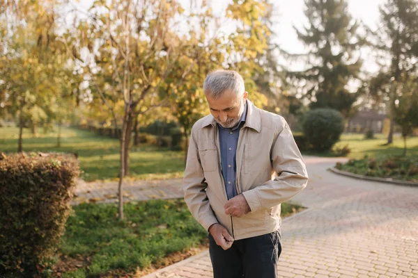 Elderly man zip a fly on jacket. Old bearded man walk in autumn park