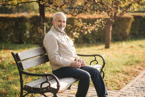 Vieil homme aux cheveux gris repose sur le banc dans le parc d'automne — Photo