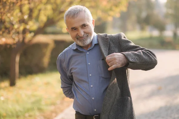 Un bel homme âgé portant une veste grise. Vieil homme barbu aux cheveux gris marche dans le parc d'automne. Fond jaune — Photo