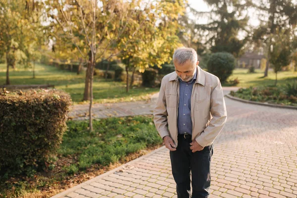 Idős ember zipzár egy légy a kabátot. Öreg szakállas ember sétál az őszi parkban — Stock Fotó