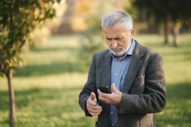 Yakışıklı sakallı yaşlı adam ceketinden bir akıllı telefon al.