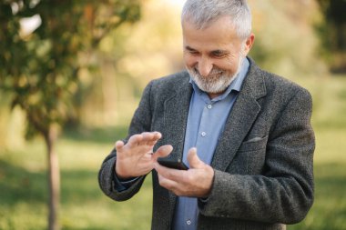 Dışarıda akıllı telefon kullanan beyaz sakallı ihtiyara yaklaş.