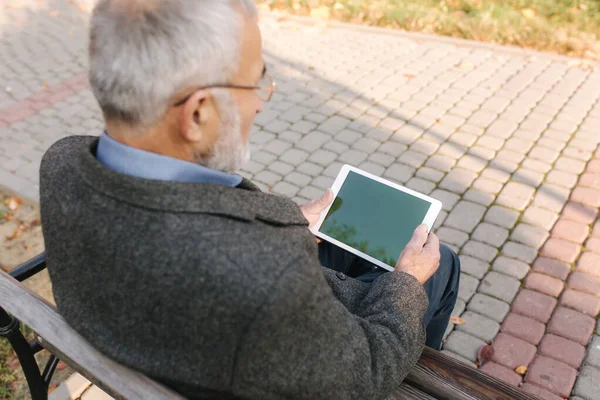 Vysmívat se staršímu muži pomocí tabletu venku. Pohled zezadu na staršího muže sedícího na lavičce a používajícího tablet — Stock fotografie