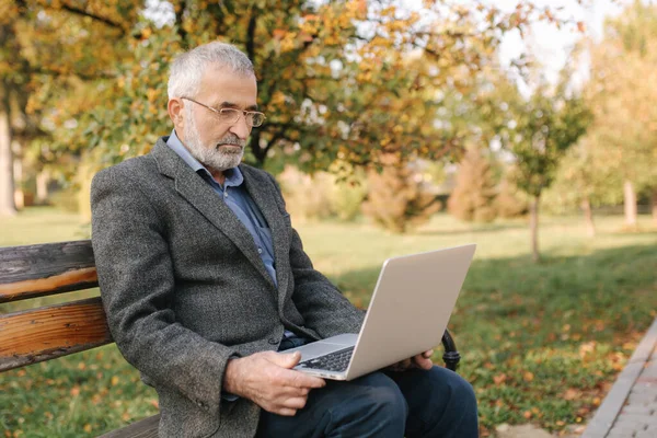高级商人在外面用笔记本电脑。 身穿灰色夹克的老人在公园里使用笔记本电脑 — 图库照片