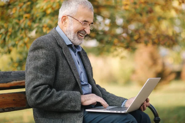 비즈니스 클래스는 노트북을 밖에서 사용 한다. 회색 자켓을 입은 노인 이 공원에서 노트북을 사용 한다 — 스톡 사진