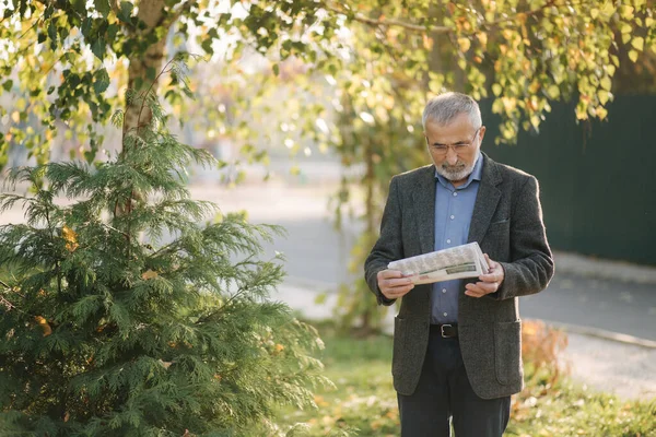 Un aîné a lu un journal dans le parc. Arrière-plan de l'arbre jaune en automne — Photo