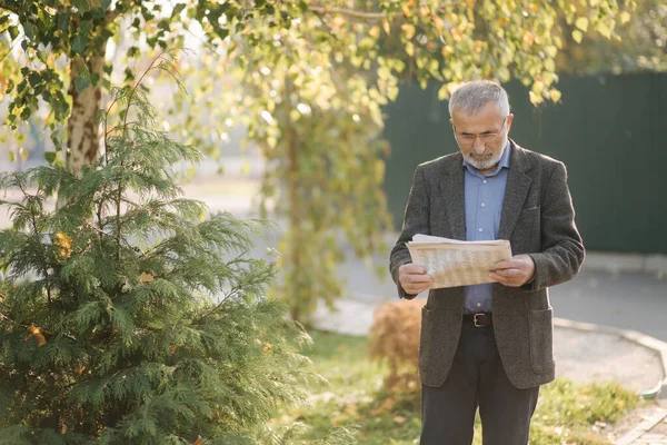 Senior man read a newspaper in the park. Background of yellow tree in autumn