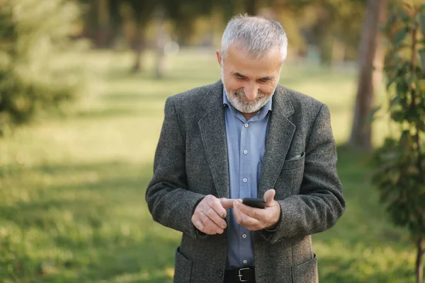 하얀 턱수염을 하고 있는 노인 과 밖에서 스마트폰을 사용하고 있는 모습 — 스톡 사진
