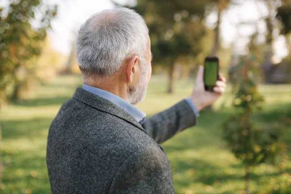 Mock up of elderly man using phone outside. Green screen. Back view of man holding phone at harms length