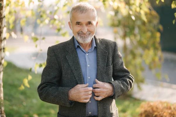 Portrait of happy elderly man in the park. Gray-haired bearded man in gray jacket — Stock Photo, Image