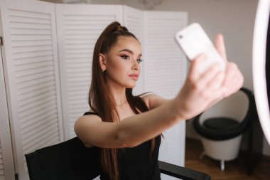 Genç çekici model güzellik stüdyosunda makyaj sonra bir selfie yapmak. Fotoğraf için yüzük lapm kullanıyor. Beyaz katlanır ekranın arka planı